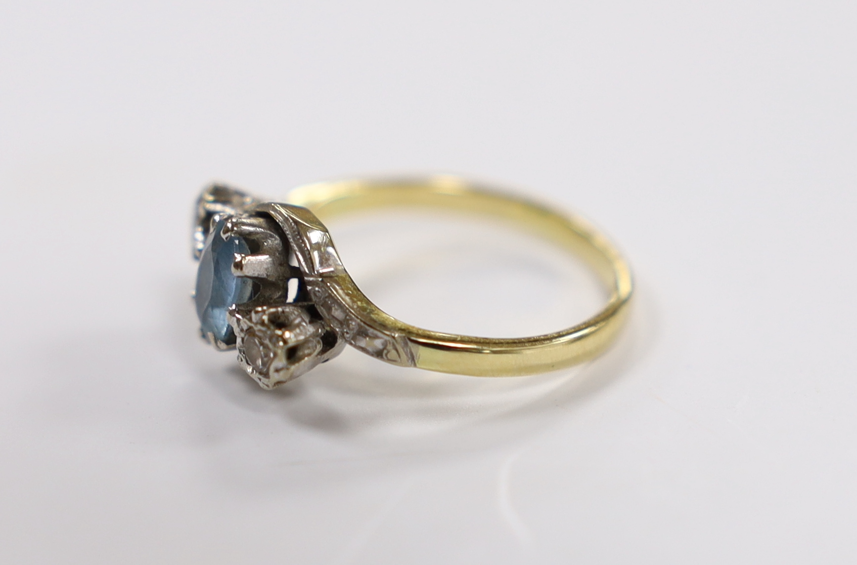 A modern 18ct gold, aquamarine and illusion set diamond three stone crossover ring, size N, gross weight 4.2 grams.